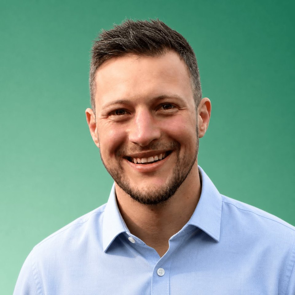 Damian van den Berg smiling in a pale blue shirt against an emerald background